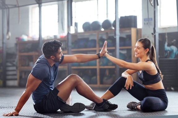 Two people sitting on an exercise mat high-five each other.