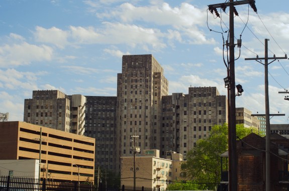 A tall, wide gray building against a pale blue cloudy sky.