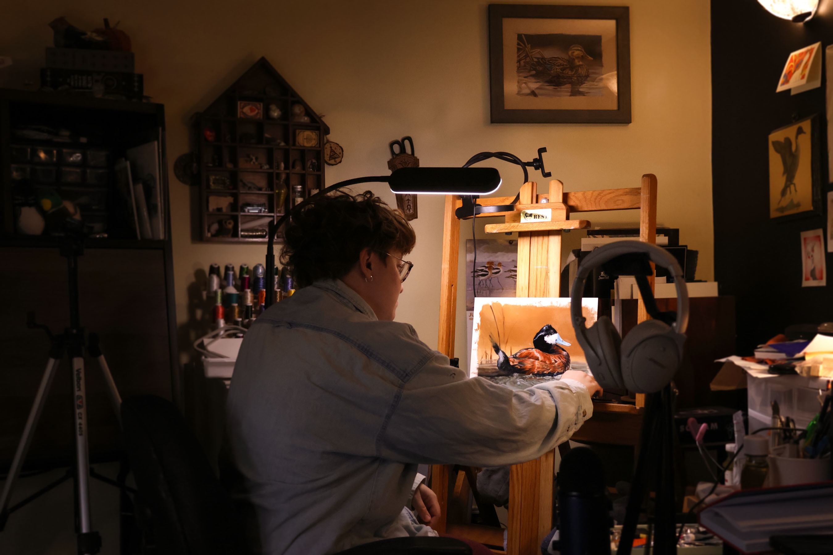 A person painting a gorgeously lit image of a ruddy duck in a home art studio.