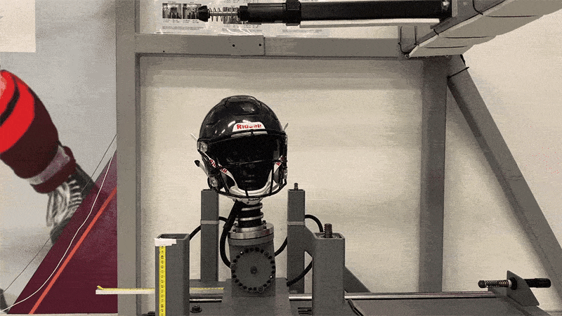 A big pendulum swings and hits a helmet on a dummy head. Concussion, sports injury testing