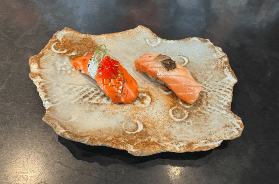 two pieces of salmon sushi, the one on the left is cultivated salmon in a lab. wildtype lab grown meat