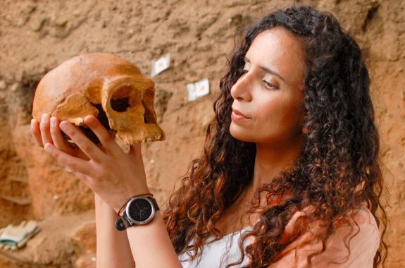 A woman holds an early human skull inside a dig site. Ella Al-shamahi, NOVA PBS Human