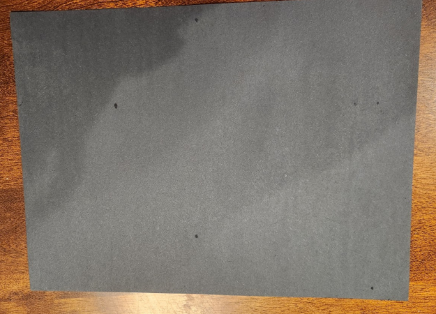 A piece of black construction paper sits on a wooden table.