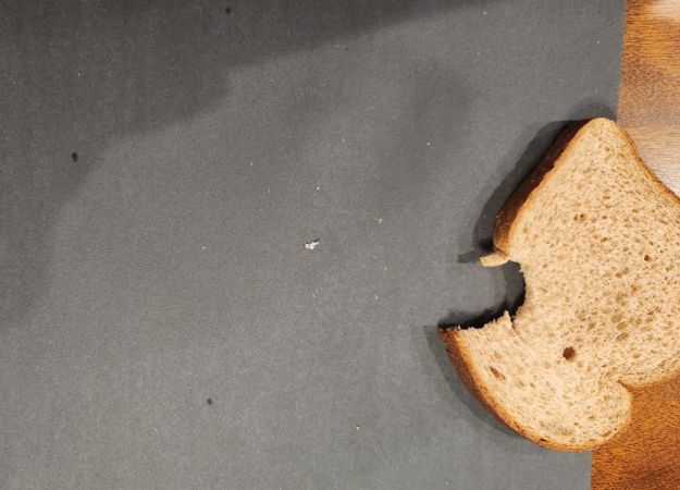 Piece of whole-wheat bread with a bite taken out sitting on a piece of black construction paper on a wooden table.