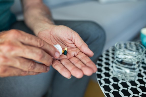 A senior man, feeling stressed and depressed, takes a pill with a glass of water. Depicting the act of self-medication and the impact of antidepressant drugs, use of medicines, SSRI withdrawal